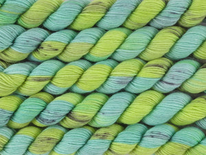 A close up of variegated bright light lime and mint greens with black speckles mini skeins of superwash merino and nylon 4ply fingering sock yarn arranged horizontally (Black Kangaroo Paw on Tough Stocking Mini)