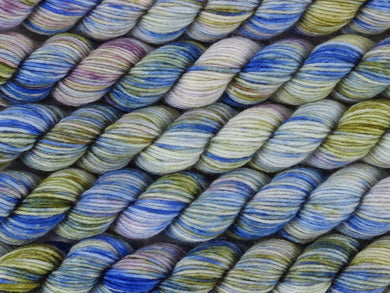 A close up of variegated cobalt blue, white, moss green and violet mini skeins of superwash merino and nylon 4ply fingering sock yarn arranged horizontally (Blue Swimmer Crab on Tough Stocking Mini)