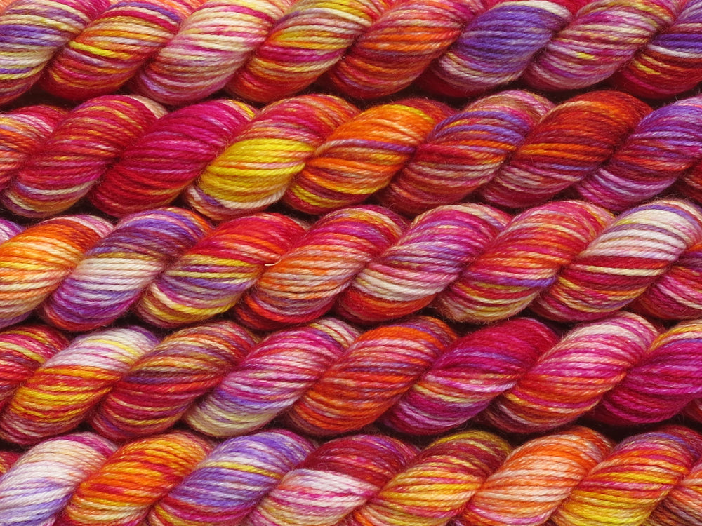 A close up of variegated white, yellow, orange, pink and purple mini skeins of superwash merino and nylon 4ply fingering sock yarn arranged horizontally (Much Ado About Knockers on Tough Stocking Mini)