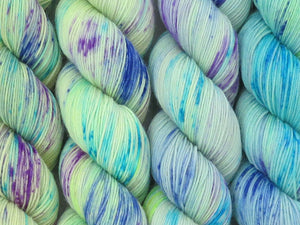 A close up of pale green yellow with speckles of blues and purple coloured skeins of superwash merino and nylon 4ply fingering sock yarn (One Hit Wonder 4 on Tough Stocking)