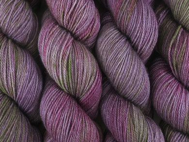 A close up of variegated purple, violet and green with hints of hot pink and beige coloured skeins of superwash bluefaced leicester, silk and cashmere 4ply fingering sock yarn (Purple Sea Urchin on Blue Chip Stocking)