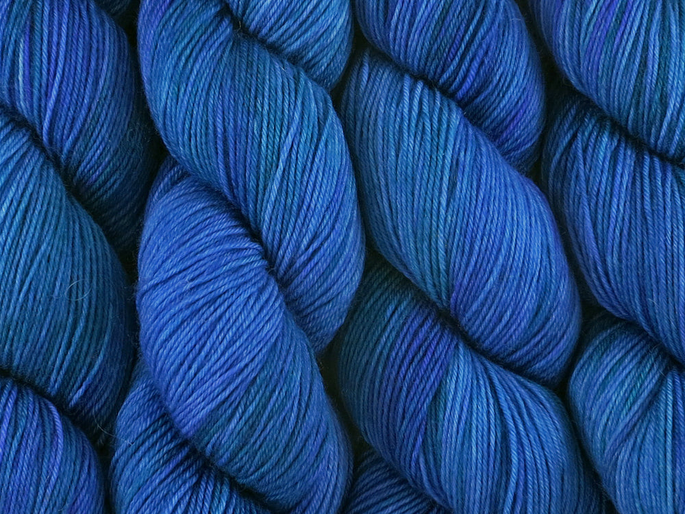 A close up of variegated medium blue with hints of teal green and blue-violet coloured skeins of superwash merino and nylon 4ply fingering sock yarn (Bass Strait on Tough Stocking)