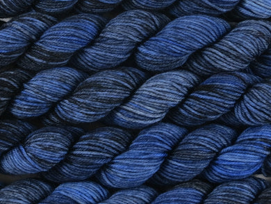 A close up of variegated yarn of black and charcoal with overtones of denim, chambray and navy mini skeins of superwash merino and nylon 4ply fingering sock yarn arranged horizontally (Moody Blues on Tough Stocking Mini)