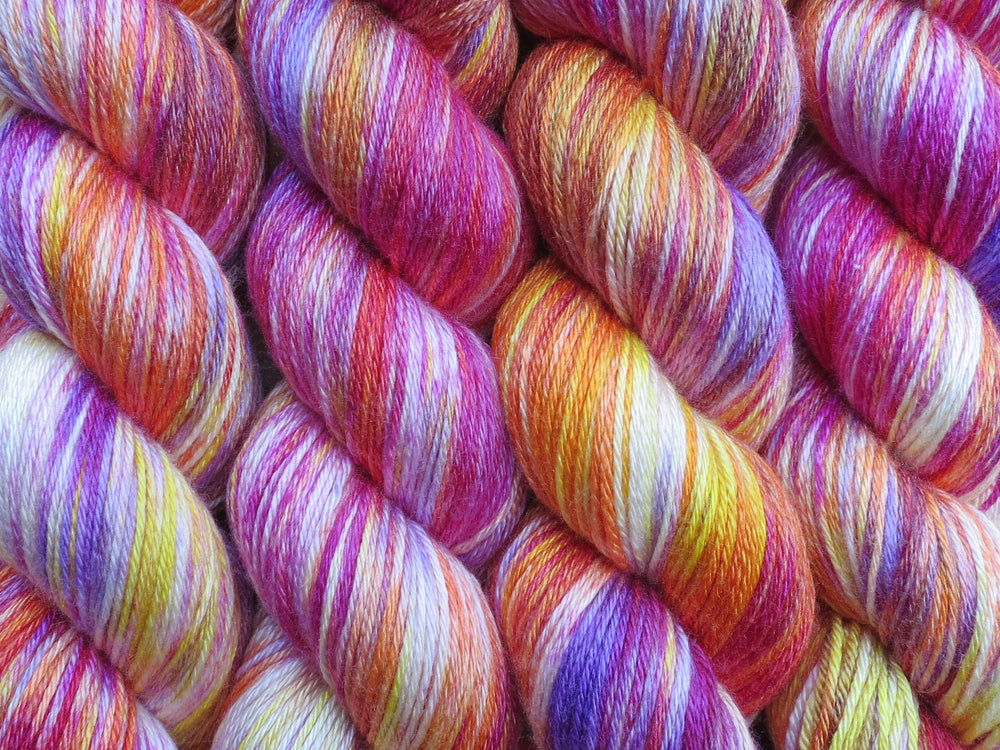 A close up of variegated white, yellow, orange, pink and purple coloured skeins of superwash merino and silk 4ply fingering sock yarn (Much Ado About Knockers on Silk Stocking)