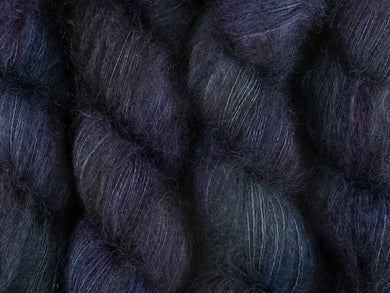 A close up of variegated black with hints of fuchsia, Kelly green and royal blue coloured skeins of superfine kid mohair and silk 2ply lace yarn (Nevermore on Kid Glove Lace)