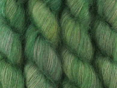 A close up of variegated light grey-green with hints of pink, sulphur yellow and deep jade green coloured skeins of superfine kid mohair and silk 2ply lace yarn (Samphire on Kid Glove Lace)