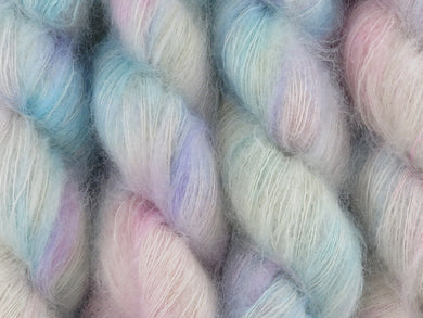 A close up of variegated white, soft pink, blue and violet coloured skeins of superfine kid mohair and silk 2ply lace yarn (White Opal on Kid Glove Lace)